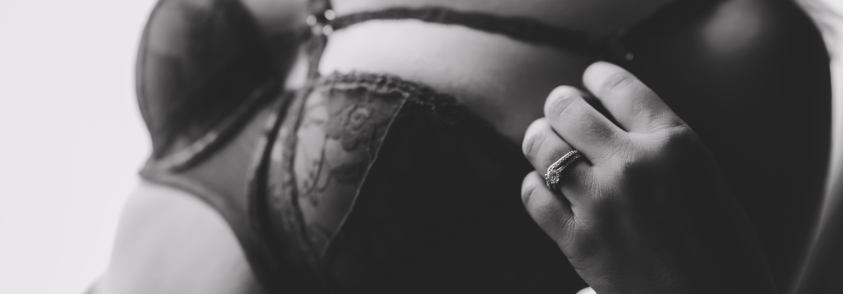 black and white close up of a woman's chest with her left hand and weddings bands in focus